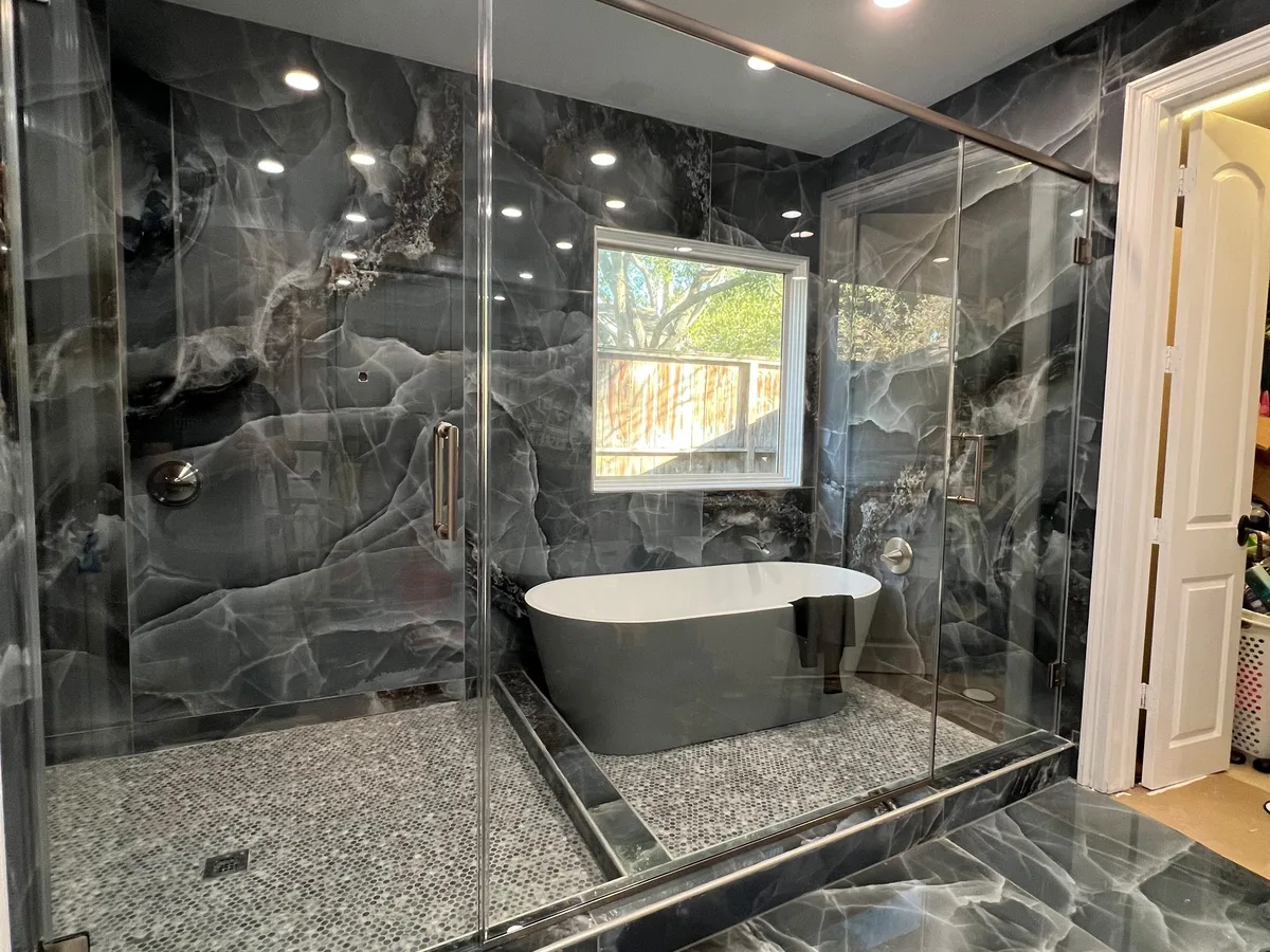 Bathroom in dark marble-look tile with a freestanding tub and glass shower