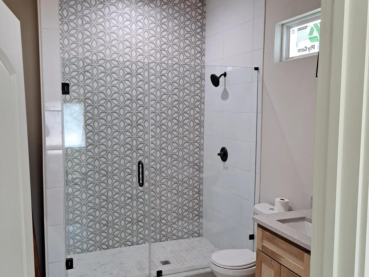 Walk-in shower with patterned tile, glass door and a wood vanity